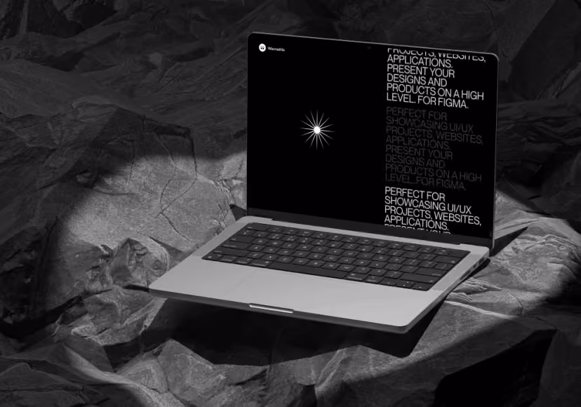 A close-up of a laptop screen showing a brutalist digital design with bold typography and a starburst graphic, set against a dark, textured rock background.